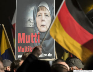 A banner reading 'Mum multiculti' and depicting a manipulated image German Chancellor Angela Merkel is carried by a protester behind the German flag as some thousands of people take part in a demonstration initiated by the Alternative for Germany (AfD) party against what they call the uncontrolled immigration and asylum abuse in Erfurt, central Germany, Wednesday, Oct. 28, 2015. (AP Photo/Jens Meyer)